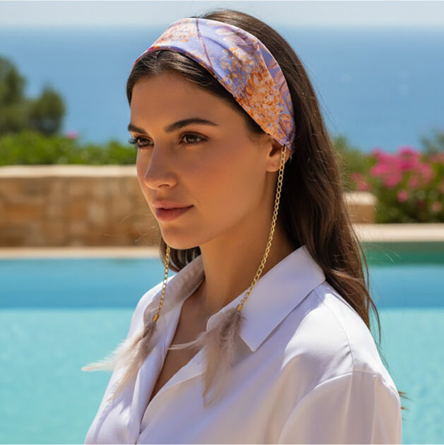 Χειροποίητη σατέν στέκα μαλλιών LILIAN με spring floral pattern σε lila και yellow αποχρώσεις, χρυσές αλυσίδες και λευκά-πούδρα φτερά. Ρομαντικό boho-chic αξεσουάρ μαλλιών για καλοκαιρινά looks.