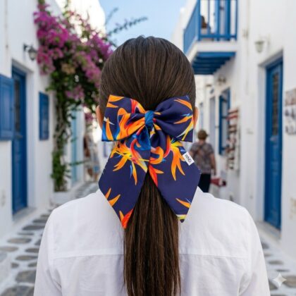 MALAGA εμπριμέ φιόγκος μαλλιών από σατέν με tropical pattern από φύλλα και φλαμίνγκο σε πορτοκαλί και μελιτζανί αποχρώσεις. Διαθέτει μπαρέτα για εύκολη εφαρμογή και σταθερό κράτημα. Εξωτικό καλοκαιρινό αξεσουάρ μαλλιών για εντυπωσιακά looks.